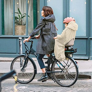 Praktisches Zubehör für Kinder auf dem Velo. Eine Frau fährt auf dem Fahrrad mit einem Kind im Kindersitz.