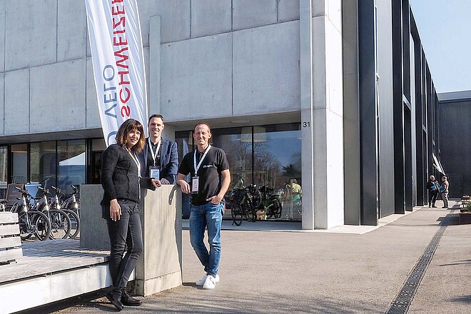 Zwei Männer und eine Frau stehen vor einem grauen Haus