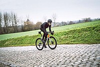 Rennradfahrer mit schwarzer Kleidung fährt über Kopfsteinpflaster