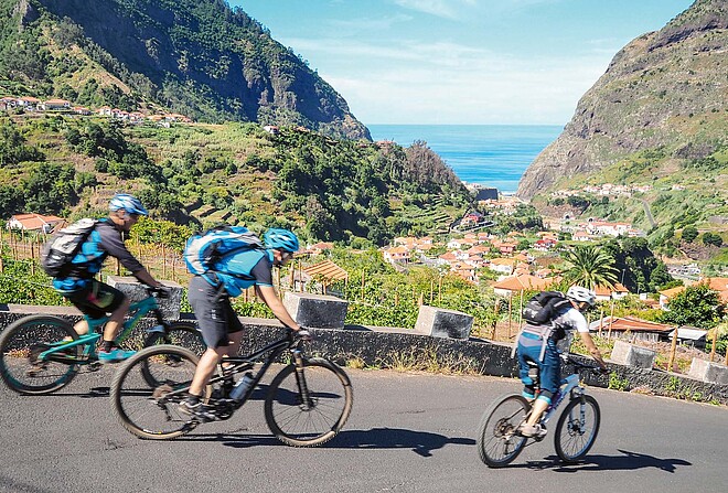 Drei Personen fahren mit Mountainbikes auf einer Strasse.
