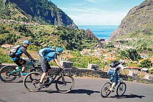 Drei Personen fahren mit Mountainbikes auf einer Strasse.