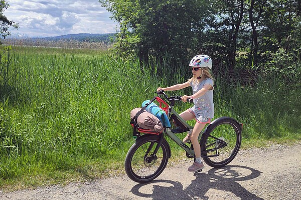 Test Woom Now 5 Kinderfahrrad. Ein Mädchen fährt mit Gepäck auf einem Kinderrad.