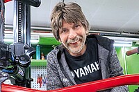 Ein Mann mit Bart steht in einer Werkstatt mit E-Bikes.