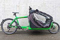 Bullitt Cargobike Test. Ein grünes Lastenrad steht vor einer Betonwand.