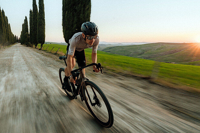 Ein Gravelbiker fährt auf einem Schotter-Weg.