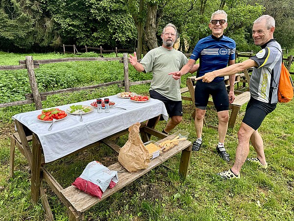 Drei Personen stehen auf einer Wiese neben einem gedeckten Tisch.