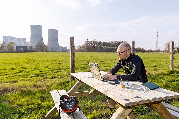 Gunnar Fehlau Workation. Ein Mann sitzt mit einem Laptop an einem Tisch. Im Hintergrund eine grüne Wiese.