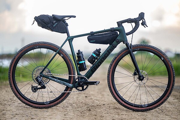 Bianchi Arcadex Bikepacking Gravelbike. Ein Fahrrad mit Taschen steht auf einer Schotterstrasse.