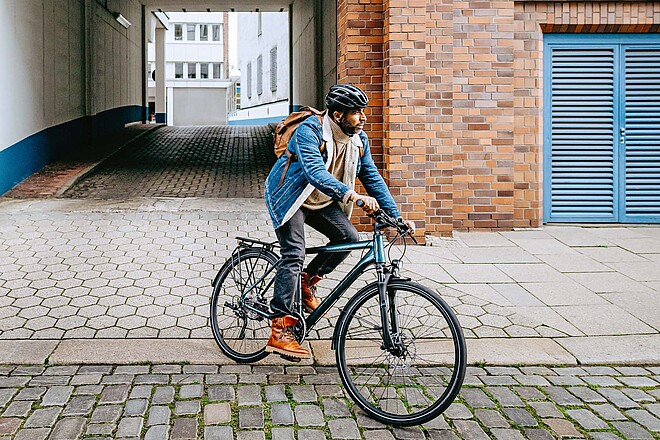 Alltagsfahrräder für weniger als 1600 Franken. Ein Mann radelt mit Jeansjacke und Helm. 
