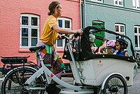Frau mit Cargobike und Kindern vor bunter Häuserzeile