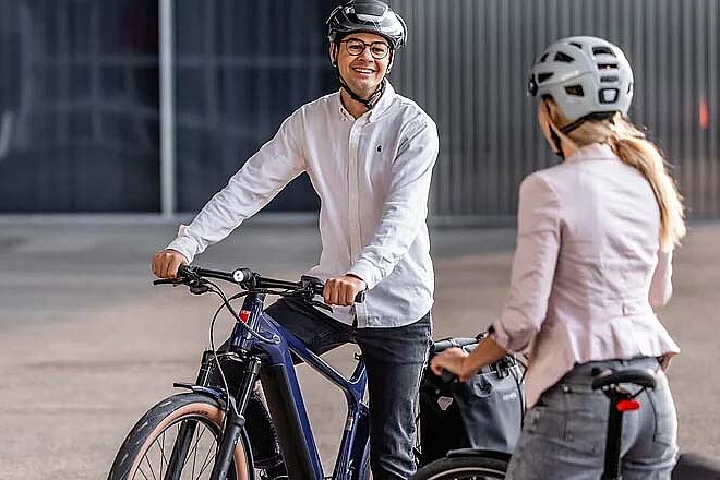 Veloplus Occasions E-Bikes. Ein Mann im weissen Hemd und mit Fahrradhelm sitzt auf einem E-Bike.