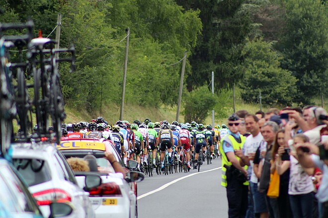 Dem Peloton folgen viele Begleitfahrzeuge. Radrennen mit vielen Zuschauern am Streckenrand