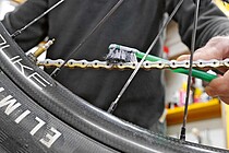 Eine Person trägt Wachs mit einer Zahnbürste auf eine Fahrradkette auf.