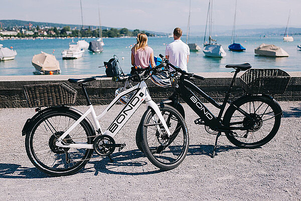 Zwei E-Bikes stehen auf einem Weg. Im Hintergrund ist ein See