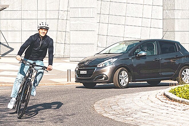 Ein Mann fährt mit dem Fahrrad durch einen Kreisverkehr, ihm folgt ein Auto.