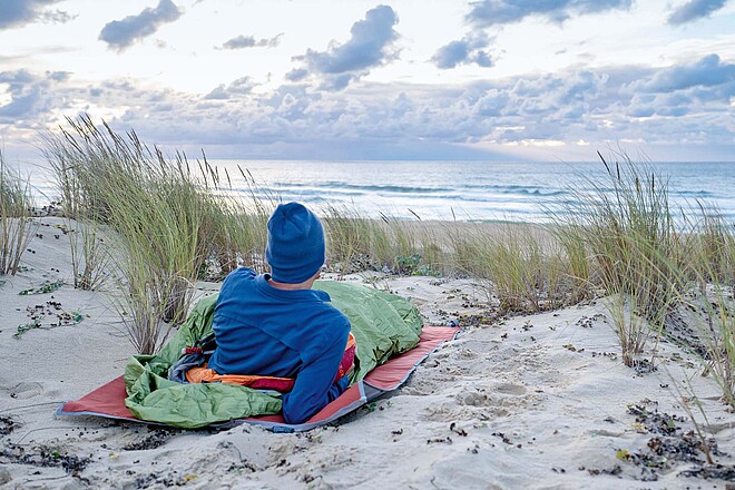Velojournal hat Biwaksäcke getestet. Ein Mann liegt in einem Biwaksack am Strand. 