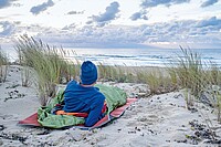 Velojournal hat Biwaksäcke getestet. Ein Mann liegt in einem Biwaksack am Strand. 