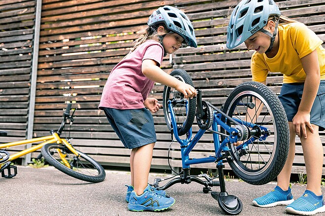 Praktisches Velozubehör für Kinder. Zwei Mädchen stehen neben einem Velo. 