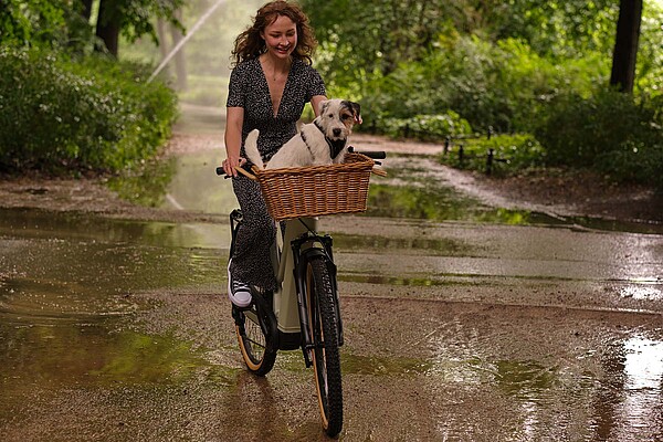 Tipps zum Kauf eines Occasions E-Bikes. Eine Frau mit Jumpsuit fährt auf einem E-Bike. Vorne ein Hund in einem Korb.