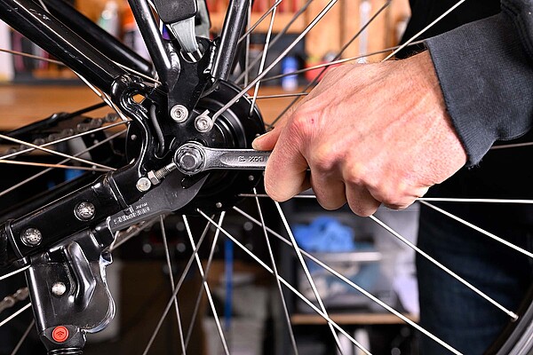 Eine Hand zieht eine Schraube am Hinterrad eines Fahrrads fest.