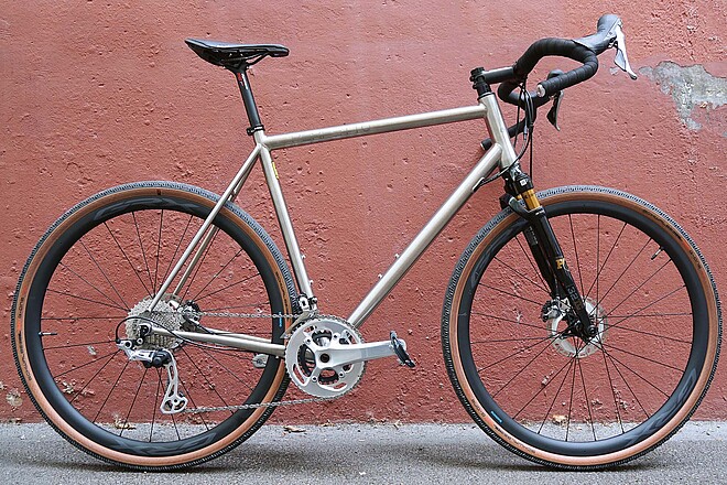 Citycycles Perfetto Gravelbike. Gravelbike aus Titan vor roter Mauer. 