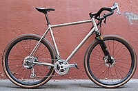 Citycycles Perfetto Gravelbike. Gravelbike aus Titan vor roter Mauer. 