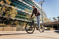 älterer Herr fährt sportlich auf einem  E-Bike entlang eines modernen Gebäudes