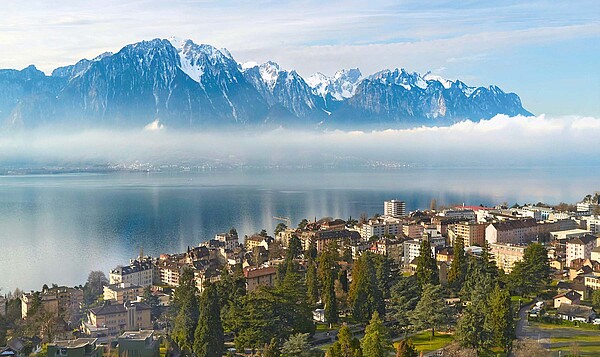Eine Stadt an einem See. Im Hintergrund Berge mit Schnee.