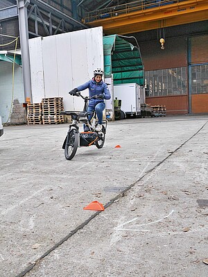 Eine Person mit Winterjacke fährt auf einem Lastenrad um Pylonen.