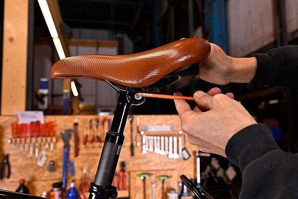 Eine Person zieht mit einem Inbussschlüssel eine Schraube an einem Fahrradsattel fest.