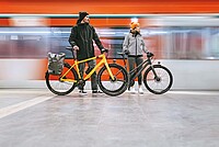 Kaufberatung Alltagsvelos. Ein Mann und eine Frage stehen mit Rädern auf einem Bahnsteig. Im Hintergrund fährt ein Zug vorbei.