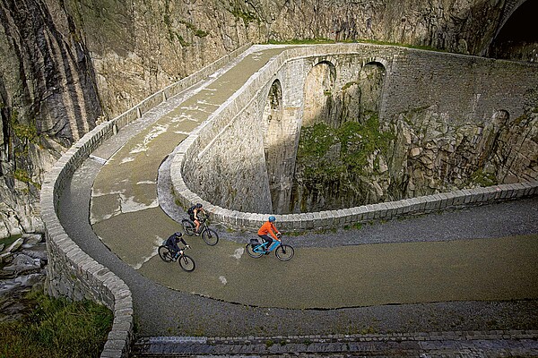 Drei Personen fahren mit Velos über eine Steinbrücke.
