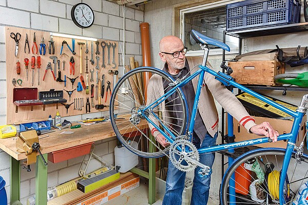 Ein Mann steht in einem Hobbykeller hinter einem blauen Fahrrad