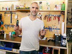 Ein Mann mit weissem T-Shirt hält eine Flasche Kettenöl in der Hand.