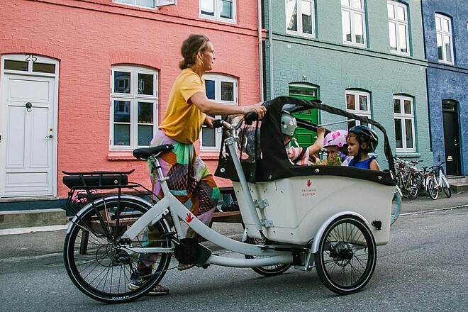 Frau mit Cargobike und Kindern vor bunter Häuserzeile