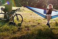 Tipps draussen schlafen auf der Velotour. Eine Frau in Fahrradbekleidung steht neben einer Hängematte.