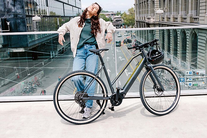 Light Support E-Bikes. Eine junge Frau lehnt lässig an einem Geländer.