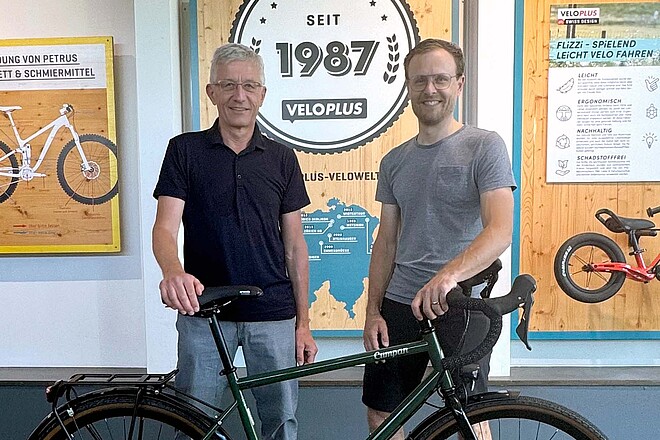 Veloplus Verwaltungsrat Wechsel an der Spitze. Zwei Männer stehen hinter einem Fahrrad.