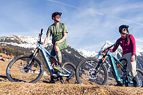 Zwei Personen stehen mit Mountainbikes auf einer Wiese in den Bergen.